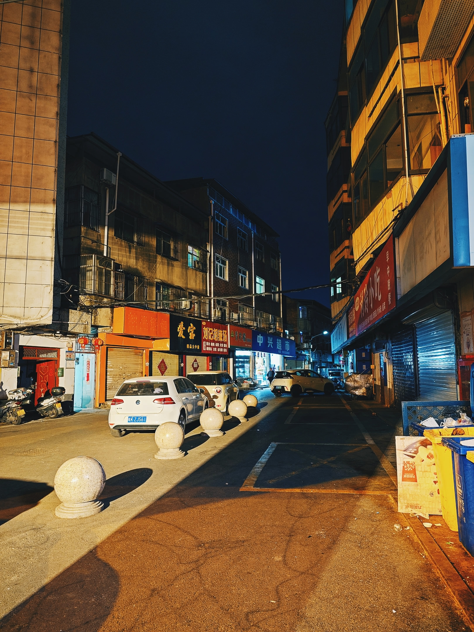 Side-street with storefronts and apartment buildings at night.