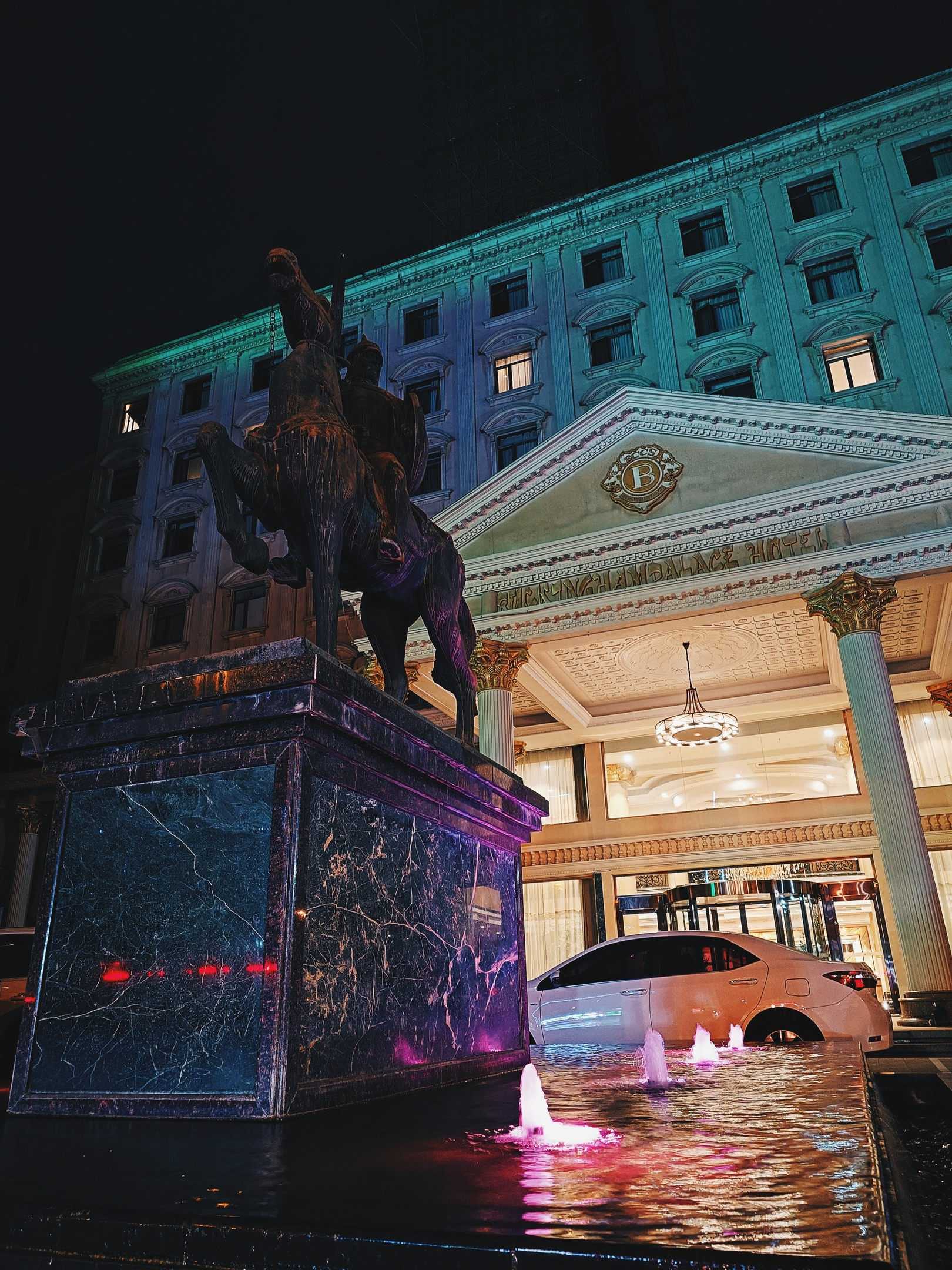 Hotel entrance with fountatin and statue of knight on horseback at night.