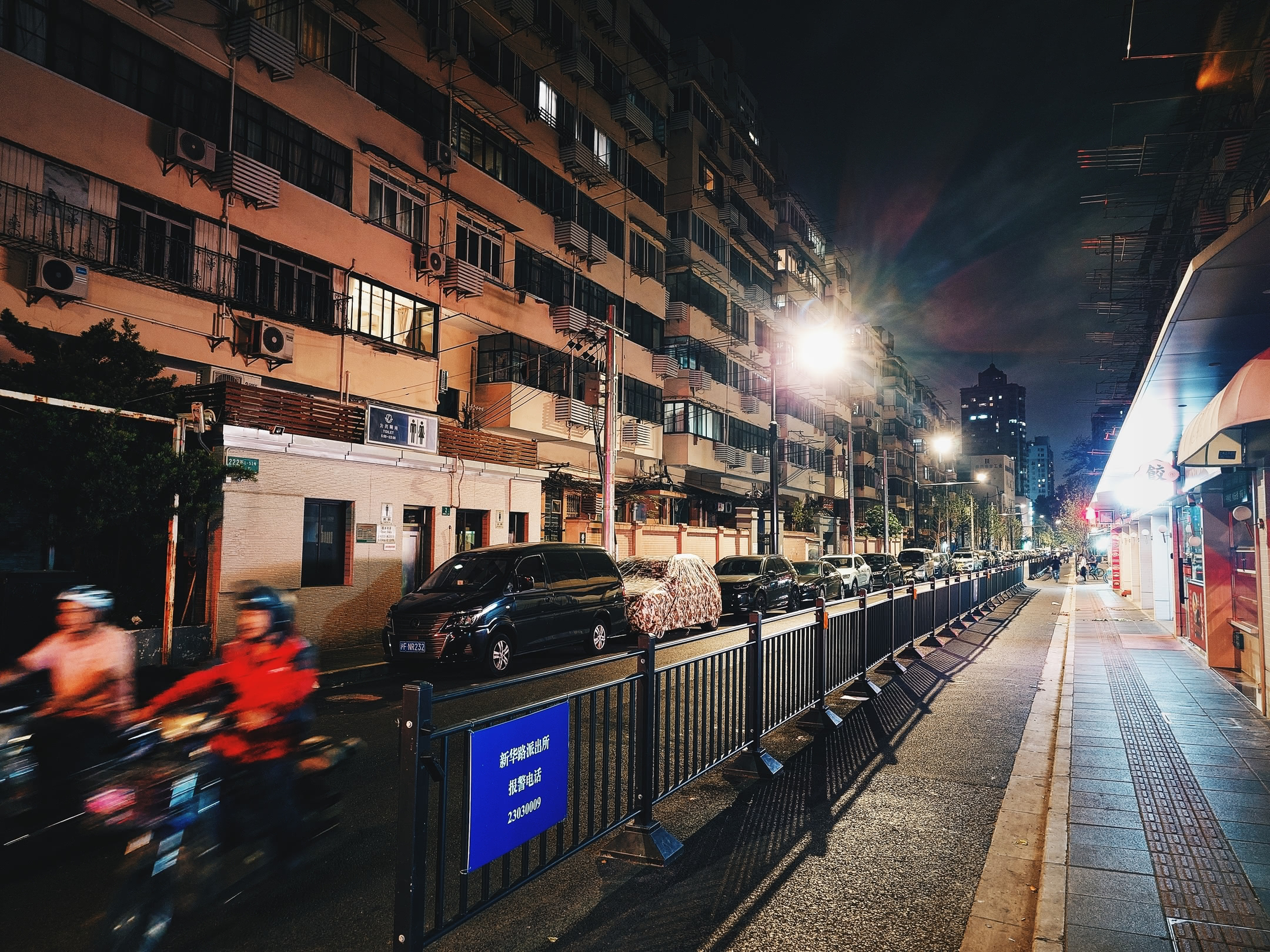 Side-street at night flanked by apartment buildings.