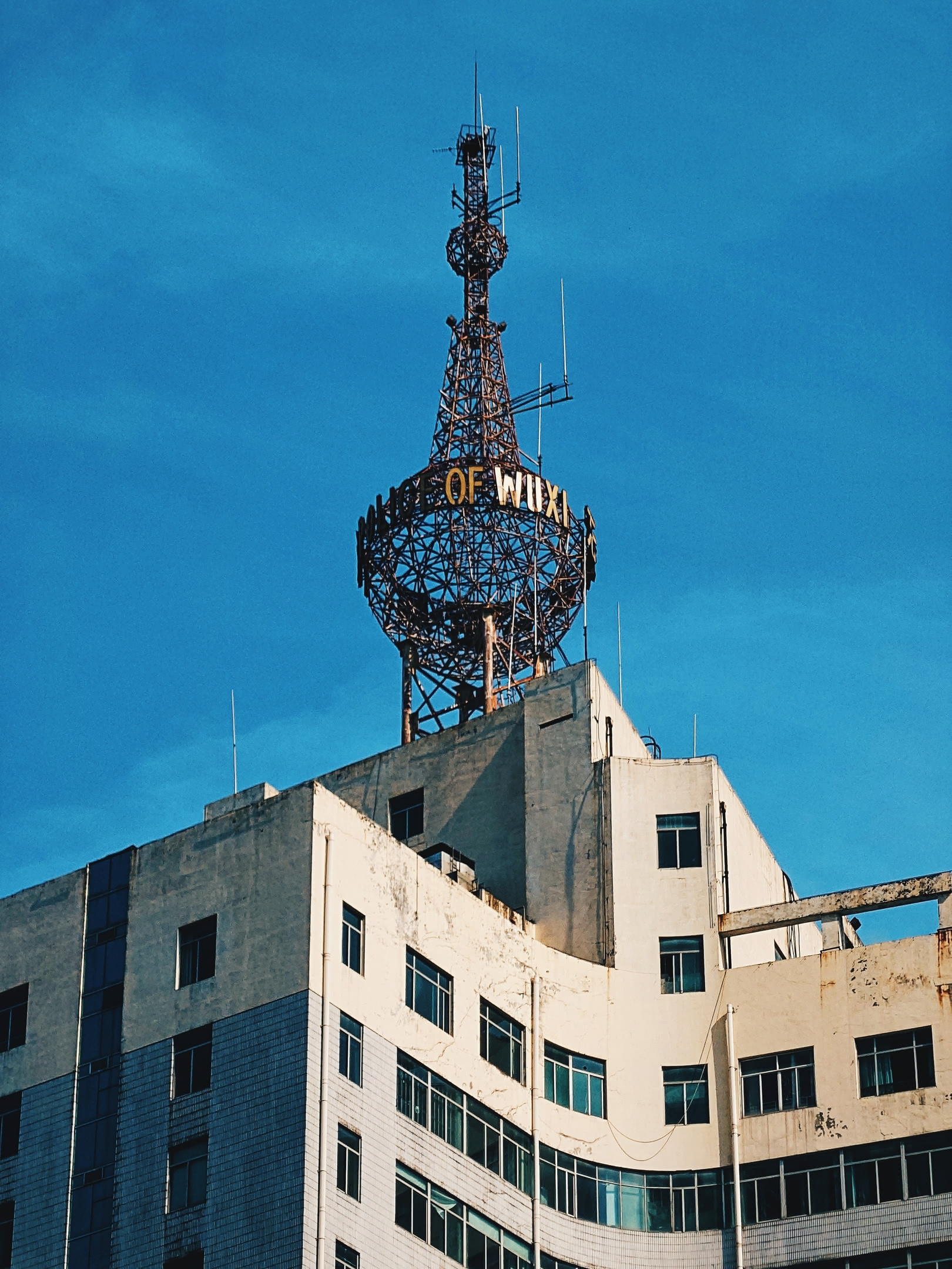 Old radio tower atop a building downtown. Wúxī city name displayed across.